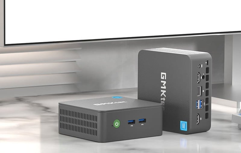 Dva mini PC GMKtec na stole vedle monitoru – jeden ležící, druhý stojící.