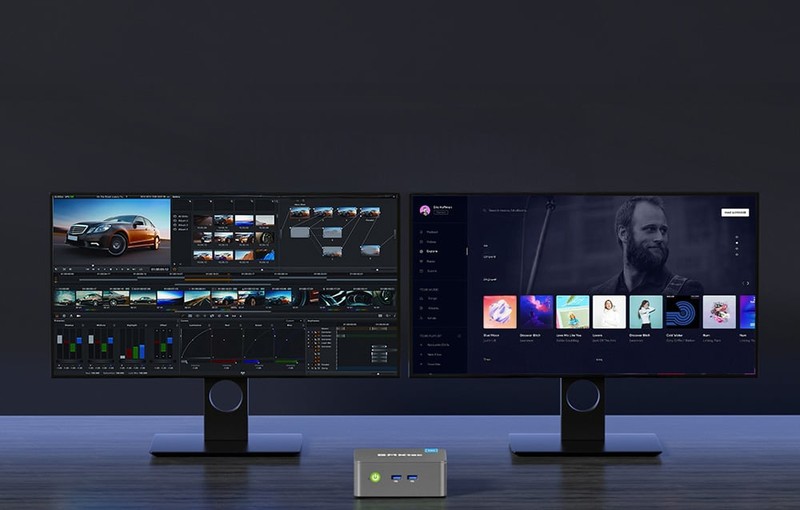 Pracovní stanice s mini PC připojeným ke dvěma monitorům zobrazujícím úpravy videa a hudební přehrávač.